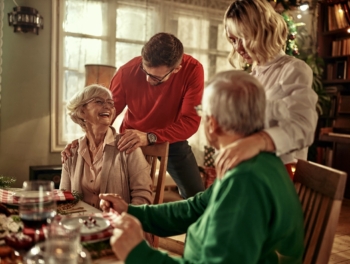 Senior couple and young adult couple hugging over Christmas dinner.