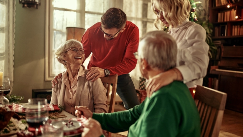 Senior couple and young adult couple hugging over Christmas dinner.